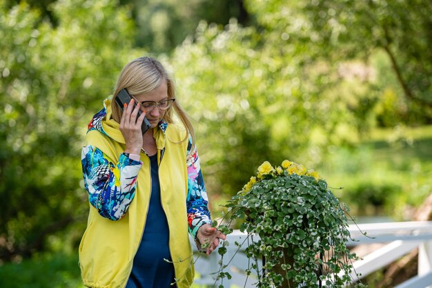 Fel geklede blonde volwassen vrouw praten op smartphone in tuin online communicatieconcept