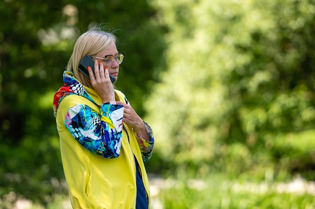 Fel geklede blonde volwassen vrouw praten op smartphone in tuin online communicatieconcept