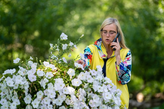 Fel geklede blonde volwassen vrouw praten op smartphone in tuin online communicatieconcept