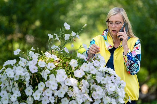 Fel geklede blonde volwassen vrouw praten op smartphone in tuin online communicatieconcept