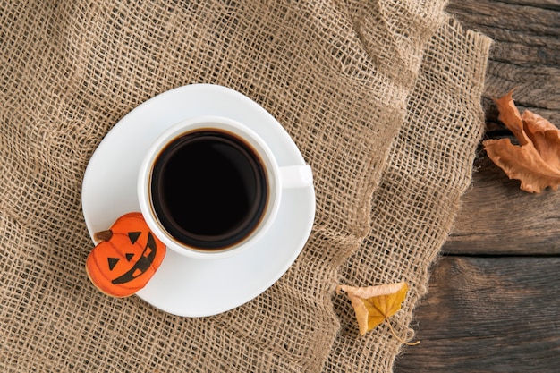 Fel oranje peperkoek-koekje-pompoen voor Halloween en een kopje zwarte koffie op een flodderig oppervlak van een houten tafel