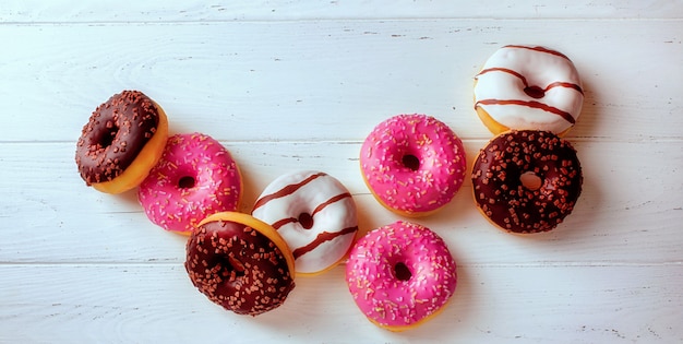 Felgekleurde donuts op een witte houten tafel bovenaanzicht, zoete gebakjes