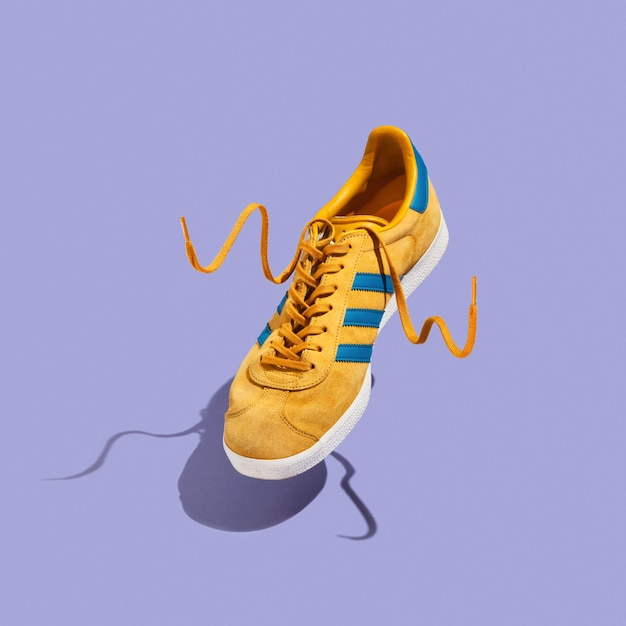 Felgele mannensneaker met blauwe strepen zweeft in de lucht Idee van sport en stijl Minimalistische trending compositie