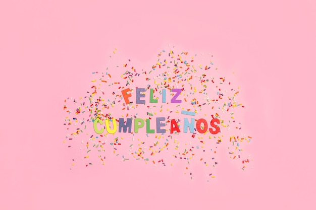 Feliz cumpleanos-groet met gekleurde hagelslag op een roze achtergrond met kopieerruimte