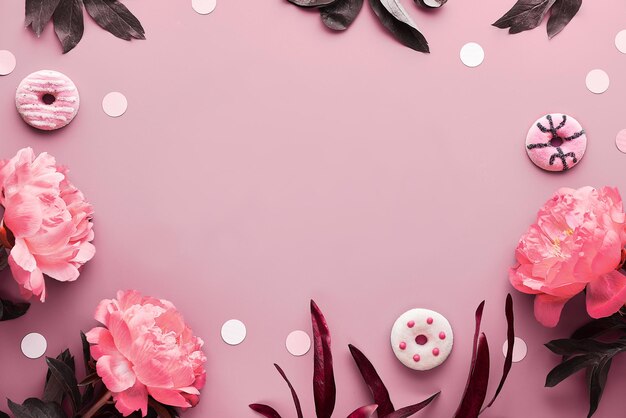 フェリスディアデラマドレはスペイン語で幸せな母の日を意味します。ピンクの牡丹の花、葉、甘いドーナツ、ドーナツ。モノクロピンクのフラワーアレンジメント。彩度の低いフラットレイ、ピンクの紙の上面図。