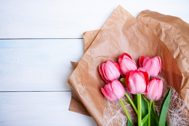 Felroze tulpen liggen op kraftpapier op een lichtblauwe houten ondergrond. Platliggend, bovenaanzicht