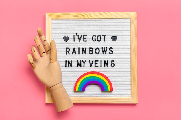 Войлочная доска, деревянная рука, радуга с цветами ЛГБТ, изолированные на розовом