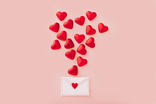 Фото Войлочный конверт с красными сердечками на день святого валентина на розовом фоне вид сверху
