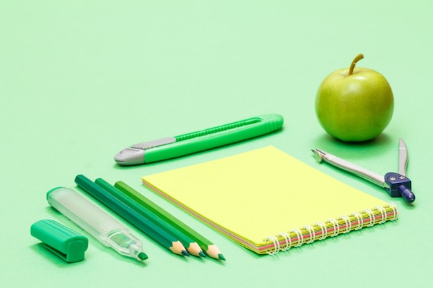 Felt pen, color pencils, a notebook, a paper knife, a compass and an apple on the green background. Back to school concept. School supplies. Shallow depth of field.