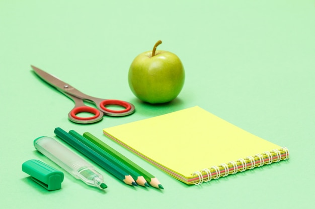 Felt pen, color pencils, notebook, scissors and apple on green background. Back to school concept. School supplies. Shallow depth of field.