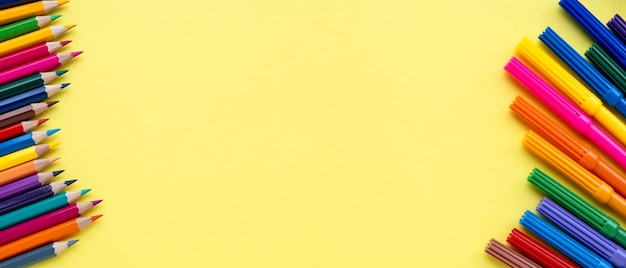 Foto penna di feltro o marcatori su un lato e una serie di matite colorate sul secondo lato ravvicinamento su sfondo giallo