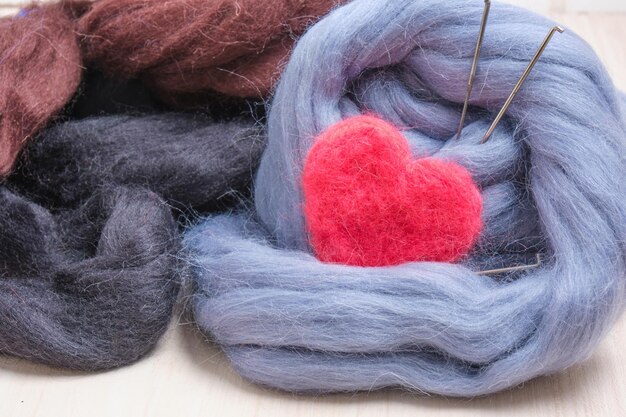 Felted woolen heart of a needle and a skein of wool on the table close up