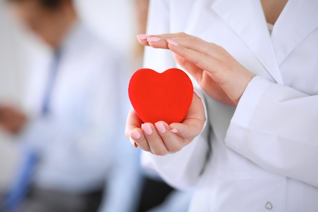 Femail doctor holding a red heart in his hands on a background of the patient. Health care concept