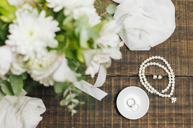 Female accessories; wedding rings ; scarf and flower bouquet on table