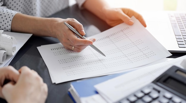 Female accountant pointing with a pen into audit paper while explaining tax counting results, close up. Business audit and finance concepts