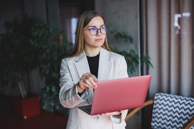 Female administrative manager in glasses and formal suit walking to office with digital laptop to check office workflow confident female business owner