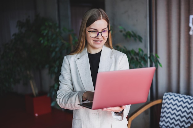 Женщина-административный менеджер в очках и строгом костюме идет в офис с цифровым ноутбуком, чтобы проверить рабочий процесс в офисе
