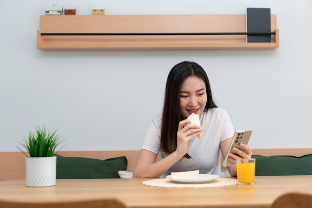 オンラインメディアを見てサンドイッチやオレンジジュースを食べることを楽しんでいる女性の大人