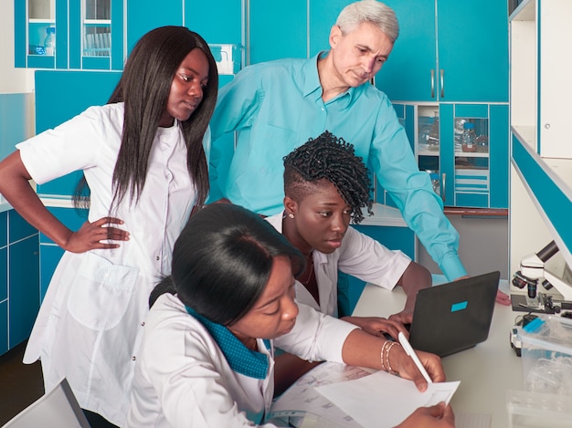 Photo female african medical students or graduates show data to caucasian man, senor group leader. looking for treatment, developing vaccine to corona virus causing covid-19. progress report in laboratory.