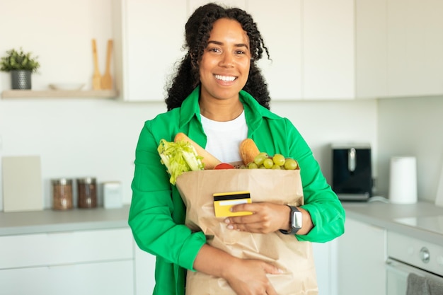 キッチンでカードとバッグを保持している食料品の買い物の後、女性