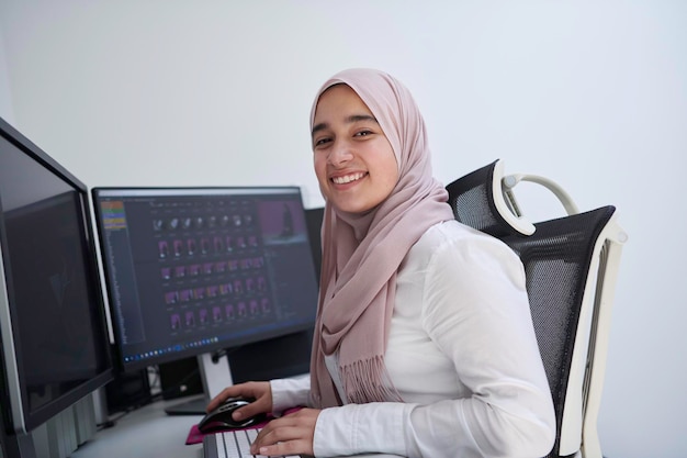 арабский творческий профессионал женского пола, работающий в домашнем офисе на настольном компьютере с двойным экраном
