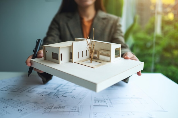 A female architect holding and working on an architecture house model with shop drawing paper in the office