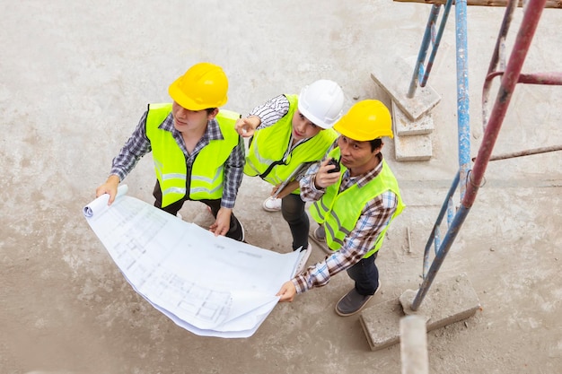 Female architect looks blueprint consults with two male workers on construction