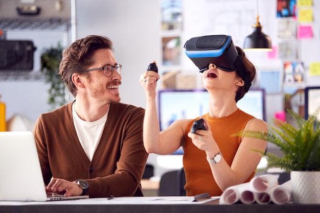 Female Architect Wearing VR Headset In Office Working With Male Colleague At Desk With Laptop