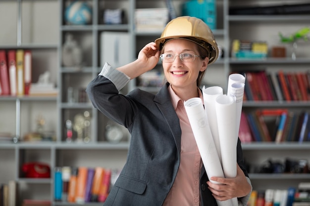 Photo female architect with blueprint in helmet on office background