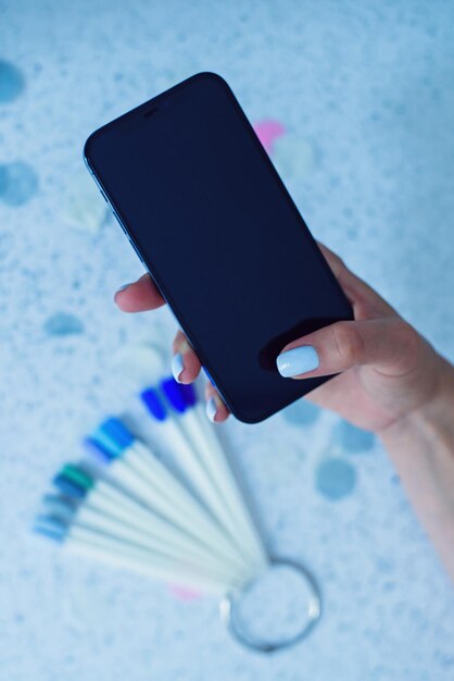 Female arm holding smartphone while sitting at manicure salon