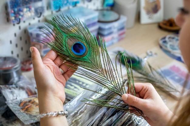 Female artist choosing natural peacock feather for creating dreamcatcher at workshop decor amulet