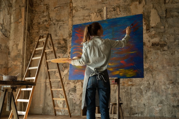 Foto l'artista femminile dipinge un'immagine del suo studio nelle sue mani sono i pennelli e una tavolozza