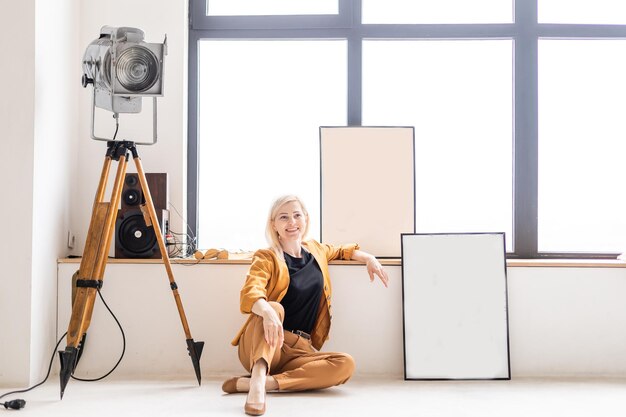 빈 캔버스 옆에 있는 스튜디오에 앉아서 웃고 있는 여성 예술가. 직장에서 여자의 초상화입니다.
