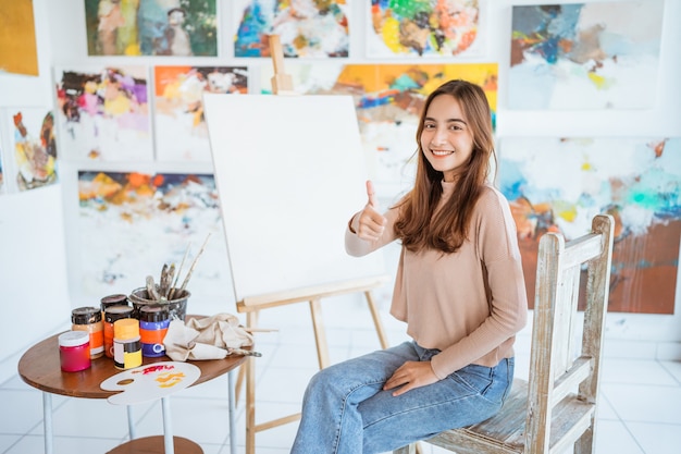 Female artist standing next to her painting and showing thumb up