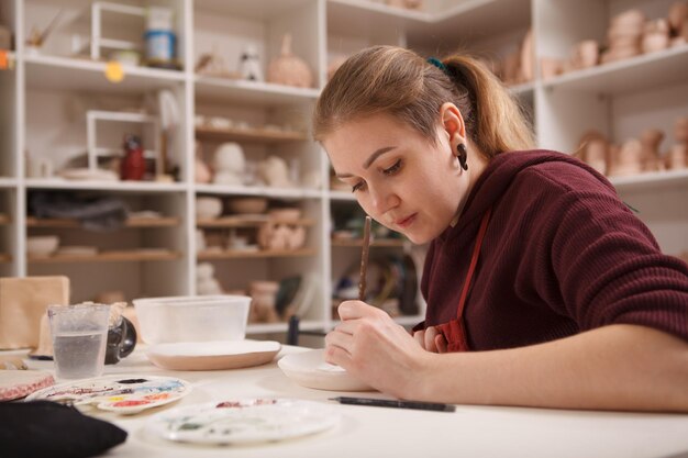 Female artist working at pottery class, painting ceramic plate, copy space