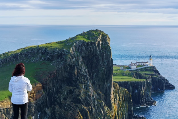 Female Asian tourist looking at the famous Neist Point Lighthouse situated in the West Coast of Skye in the area known as Durinish , Isle of Skye , Scotland