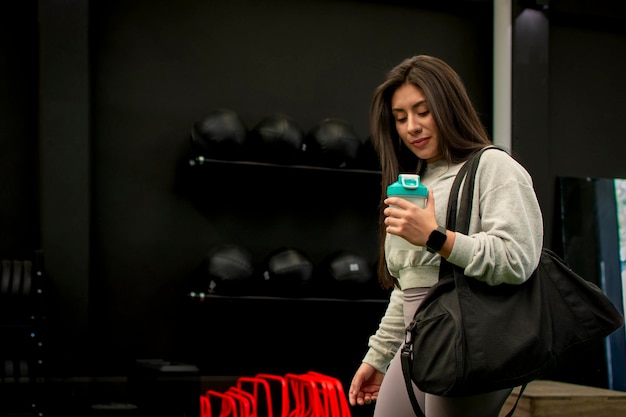 사진 여자 운동 선수 가 체육관 에 도착 하고 스포츠 가방 과 <unk>기 를 들고 웨이트 트레이닝 을 하고 있다