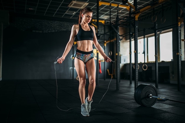 Female athlete exercise with a jump rope in sport gym. Active woman workout in fitness club