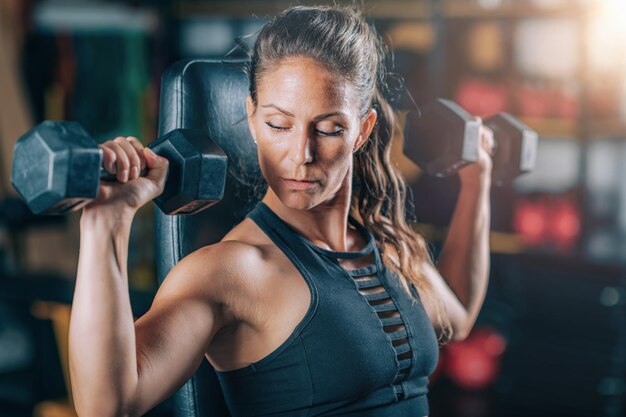 Female athlete exercising with dumbbells in the gym strength training