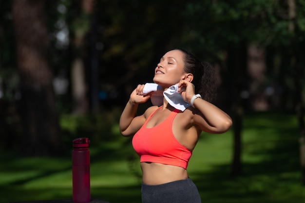 Atleta femminile sta con un asciugamano e una bottiglia d'acqua prendendo il sole dopo un allenamento all'aperto
