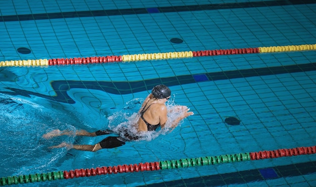 女性アスリートがプールレーンでブレストスタイルで泳いでいます