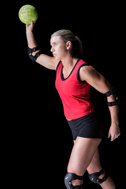 Female athlete with elbow pad throwing handball on black