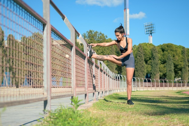 Female athlete with tattoos performs stretching in a park in a sunny day