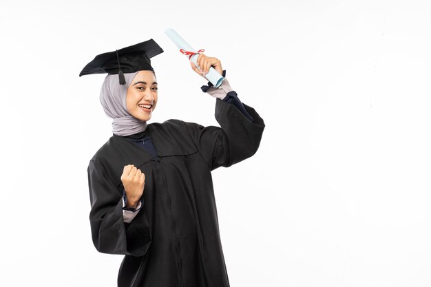 Female bachelor graduate wearing toga with hand clenched while holding a roll of diploma paper standing on isolated background