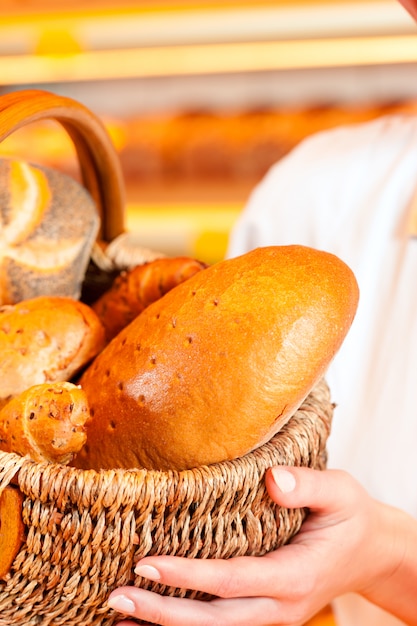 Female baker in bakery selling bread by basket 