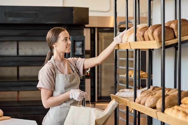 Female baker or clerk taking loaf of fresh bread from display