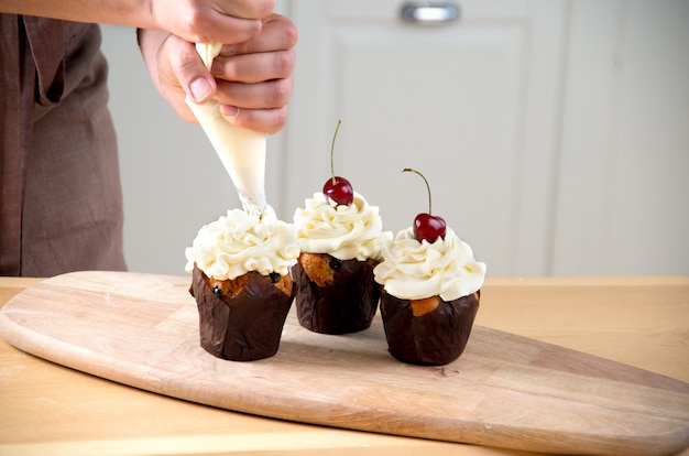 Foto panettiere femminile che decora cupcake con ciliegia e crema