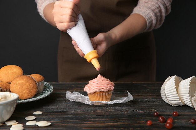 Фото Женщина-пекарь украшает вкусный кекс кремом за столом