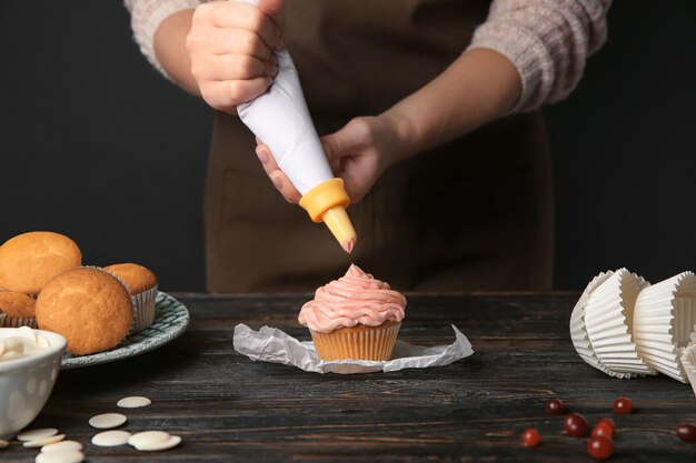 写真 テーブルでクリームとおいしいカップケーキを飾る女性のパン屋