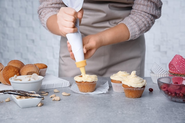 Female baker decorating tasty cupcake with cream at table